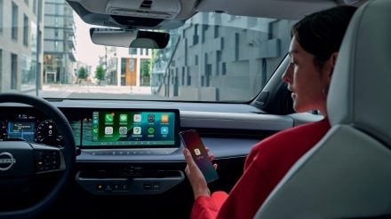 Nissan LEAF ekrāns un sieviete, kas tur viedtālruni.