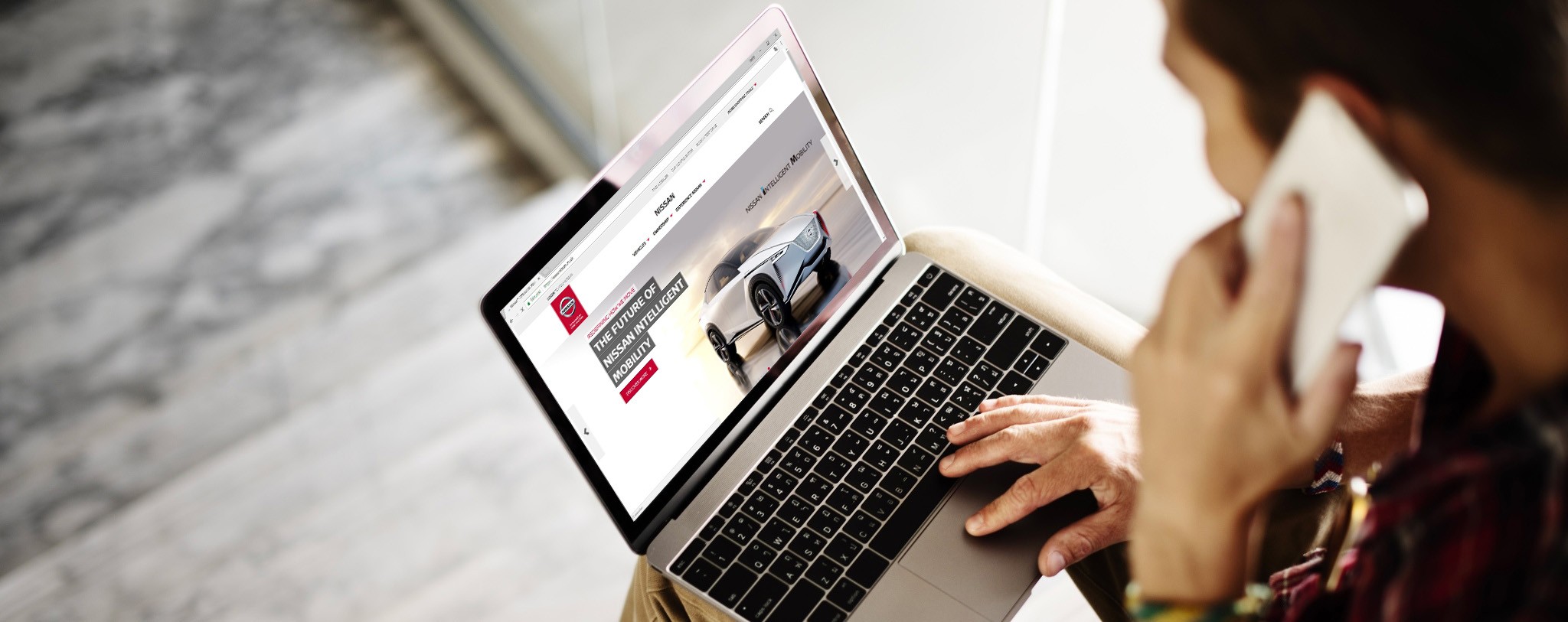 Nissan verkkosivut auki tietokoneella sekä henkilö puhelimessa