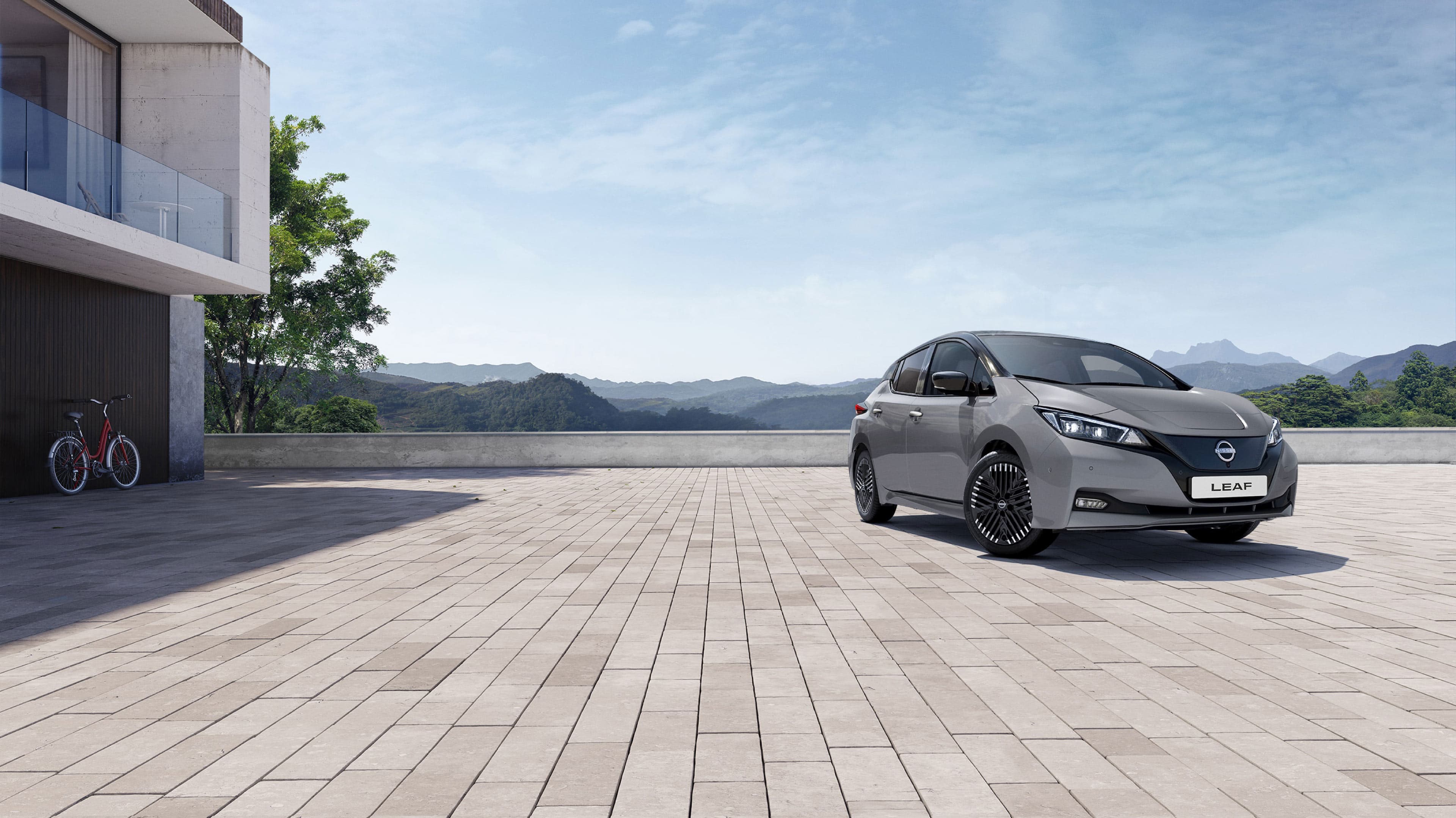 Bilde av en grå Nissan Leaf elbil som står parkert foran et funkishus med glassveranda