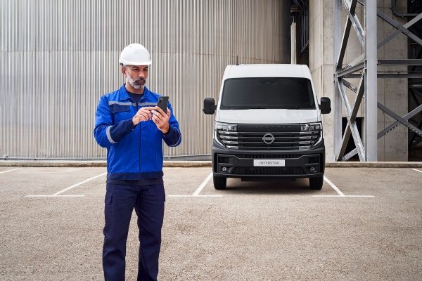Nissan Van line-up: Full front view of parked Interstar in front of warehouse and a workman standing in front using his phone