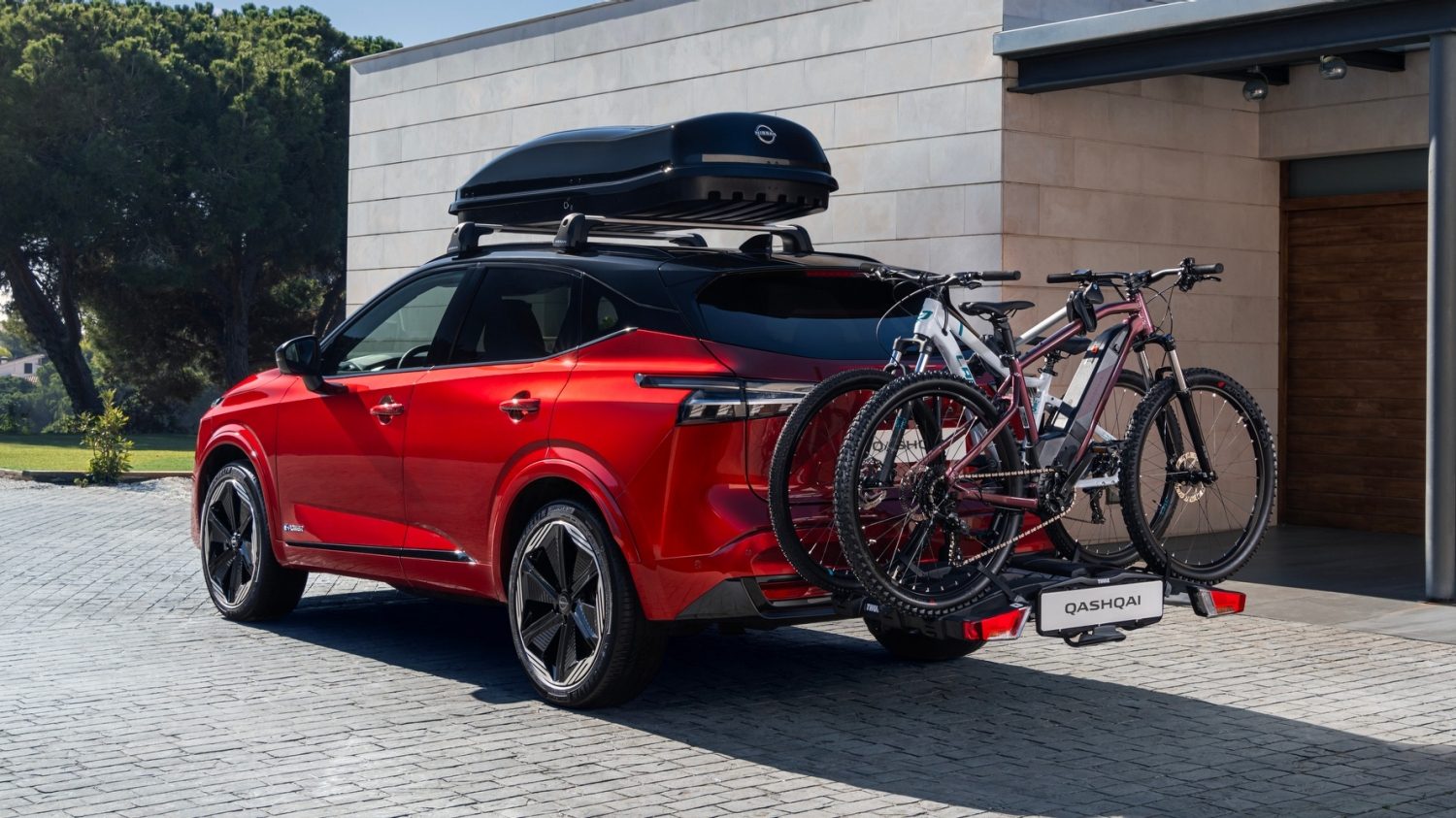 Rød Nissan Qashqai SUV parkeret foran moderne hus med cykelholder og to mountainbikes bagpå samt tagboks – tilbud på tilbehør og reservedele