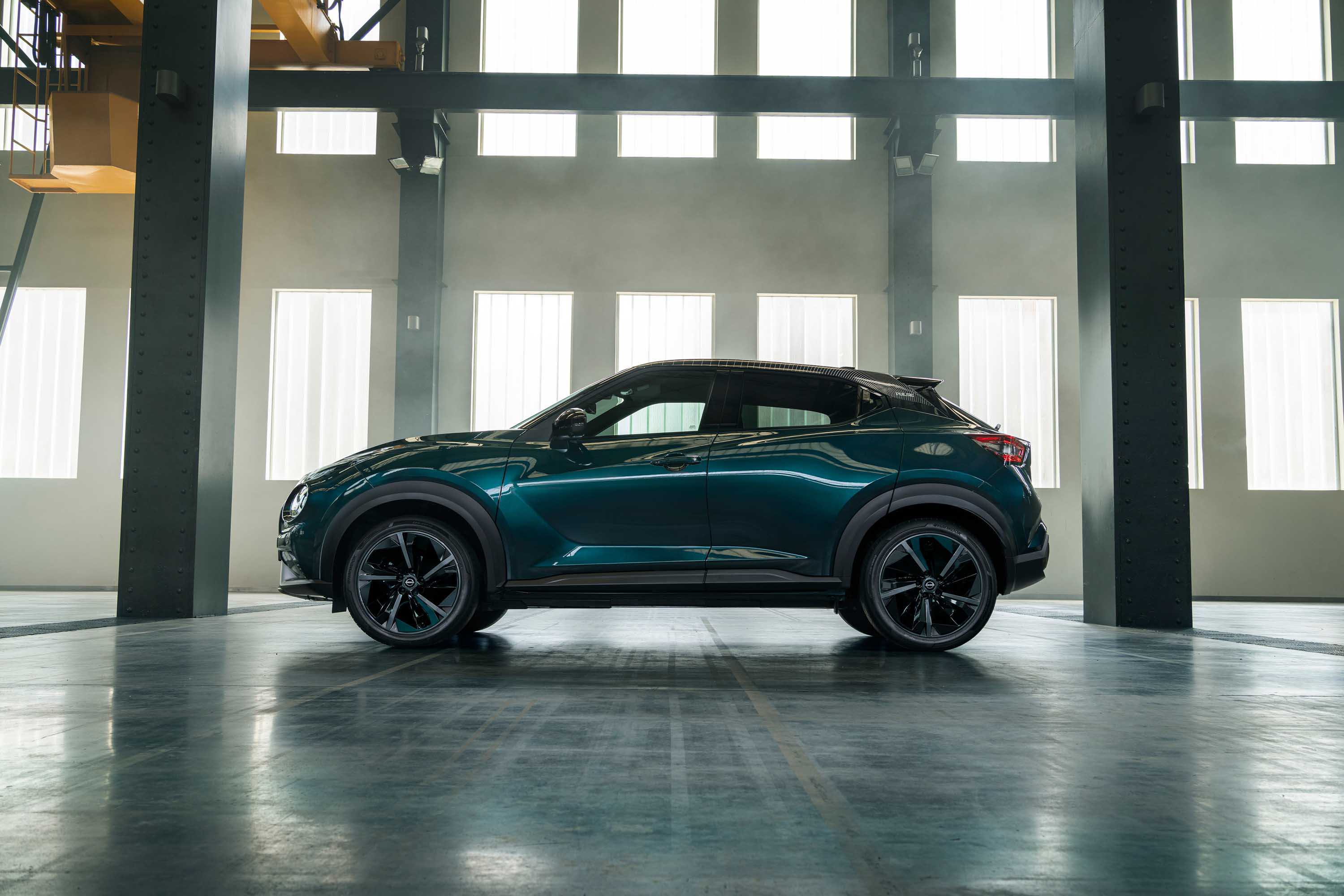 Profilvy av Nissan JUKE Hybrid SUV parkerad bredvid affär med person som står utanför och håller en telefon