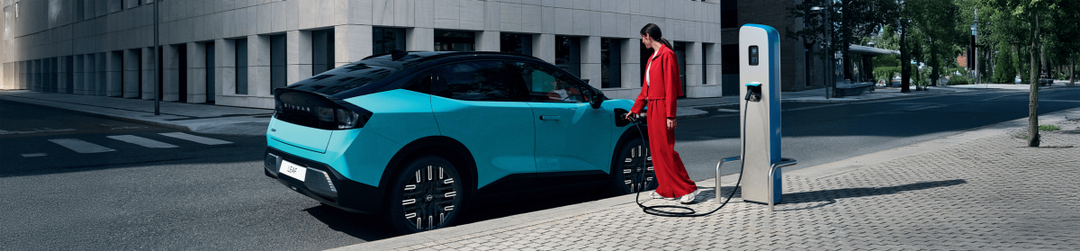 Turkizni Nissan Leaf vozilo med polnjenjem na javni polnilni postaji v mestnem okolju.