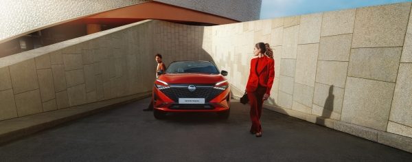 Rdeči Nissan Qashqai vozilo sprednji pogled na urbanem parkirišču ob kamnitih zidovih.