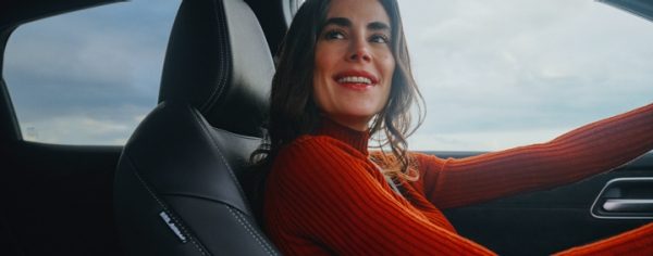 Nissan vozilo, unutrašnjost s tamnim sjedalima, žena u narančastom džemperu na suvozačevom sjedalu
