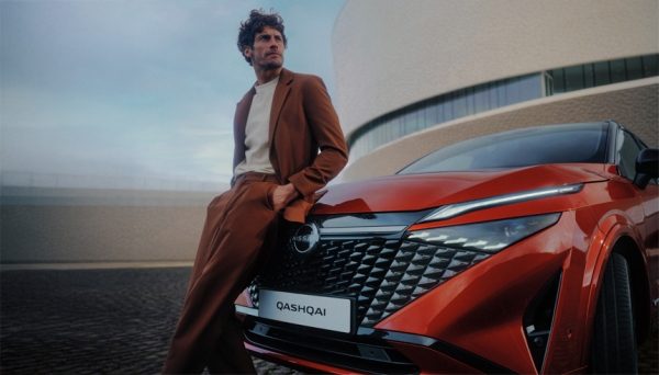 Rdeči Nissan Qashqai vozilo sprednji pogled z detajlom LED žarometov in maske pred sodobno arhitekturo.